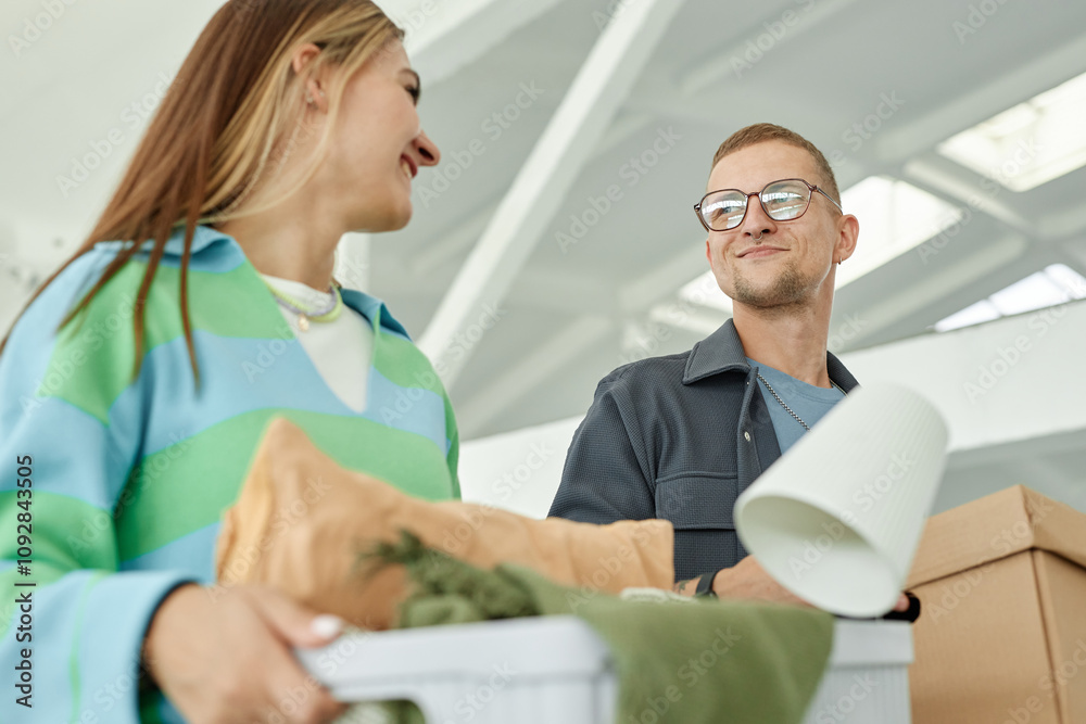 Medium shot of smiling man looking at cheerful girlfriend carrying boxes with personal belongings to self storage warehouse, while donating items to charity or moving out Medium shot of smiling man looking at cheerful girlfriend carrying boxes with personal belongings to self storage warehouse, while donating items to charity or moving out