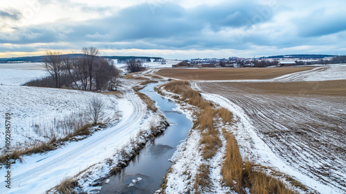 Winter plowed field with small river European nature agriculture concept. Rural nature scenery landscape. Cold weather winter landscape with snow and ice