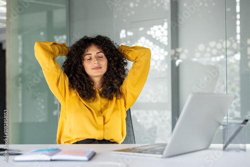 Young woman takes relaxing break at desk with laptop, enjoying moment of peace. Concept of workplace relaxation, mental health at work, and stress relief.