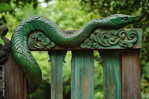 Green wooden snake sculpture is adorning a rustic gate with a green leafy background photo