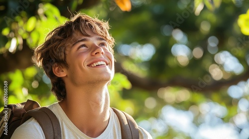 A young man smiles while looking up, surrounded by lush greenery and soft sunlight.