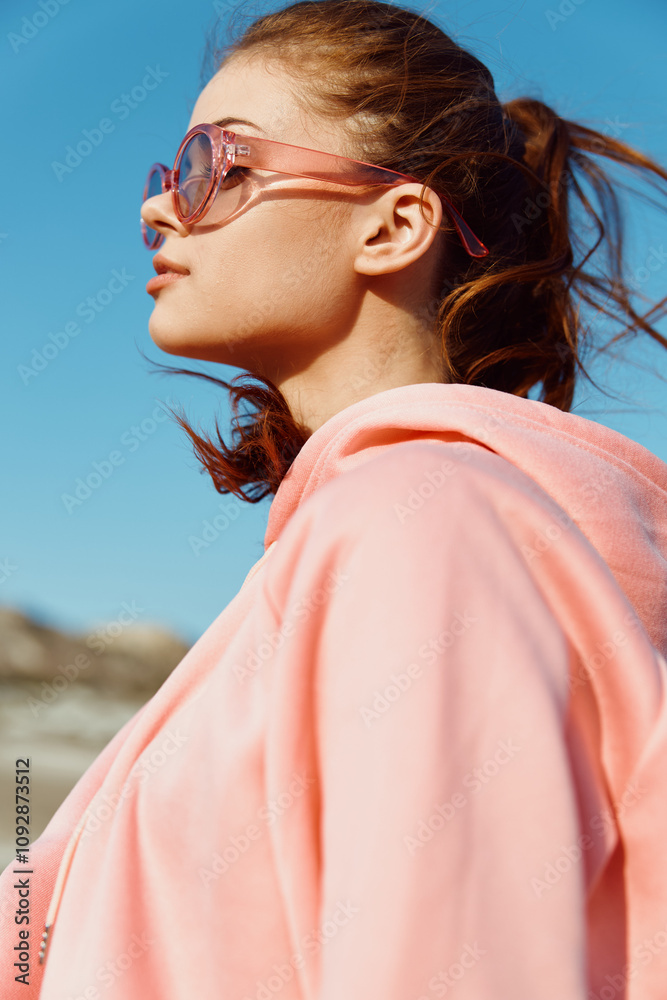 stylish woman in pink hoodie and sunglasses enjoying a sunny day at the beach with ocean view stylish woman in pink hoodie and sunglasses enjoying a sunny day at the beach with ocean view