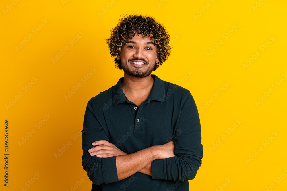 Young man with curly hair stands confidently against vibrant yellow background in stylish black shirt Young man with curly hair stands confidently against vibrant yellow background in stylish black shirt