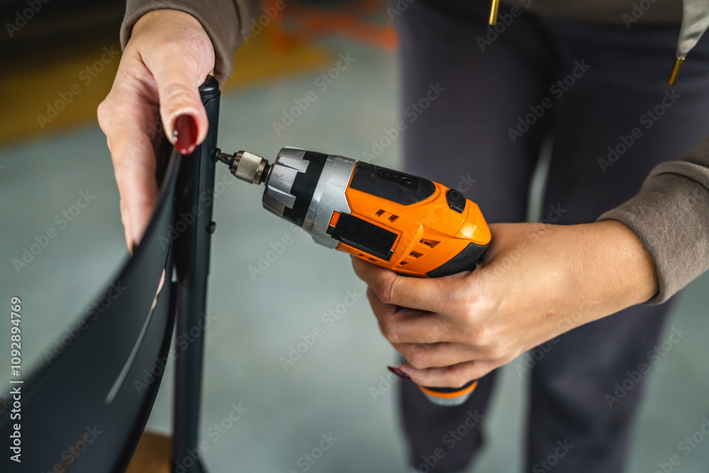 Naklejka premium close up of woman use electric screwdriver on black metal chair