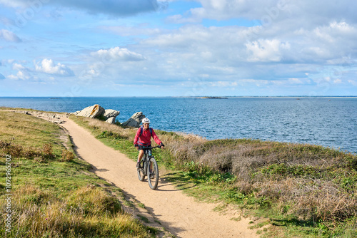 active senior woman cycling with her electric mountain bike at the wild coast of Quiberon peninsula, Brittany, France