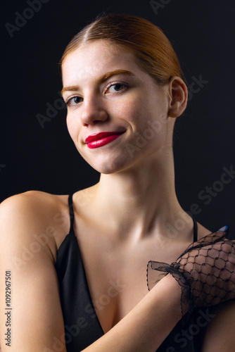 A young redhear girl with clean skin wearing black gloves. Beauty portrait of a woman on a black background in the studio. photo