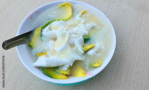 Es Oyen in a white bowl on a table is a popular drink from the city of Bandung filled with several fruits such as avocado, young coconut,and sago pearls, jelly,then mixed with sweetened condensed milk photo