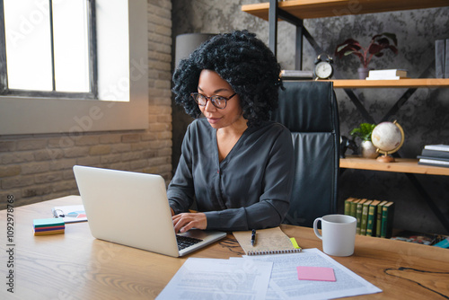 African woman in eyeglasses sit at desk staring at laptop screen, learn new software, makes assignment, working looks concentrated search solution or ideas. Business challenge thinks over task concept