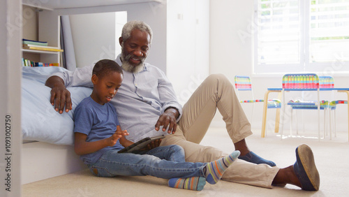 Grandfather Sitting With Grandson In Child's Bedroom Using Digital Tablet Together