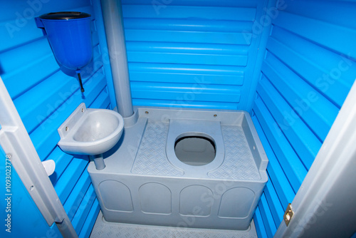 Interior dry closet with plastic blue walls. Sink with mechanical tank inside toilet. Toilet cubicle for placement on construction site. Portable dry closet. Interior toilet with anti-vandal plastic photo
