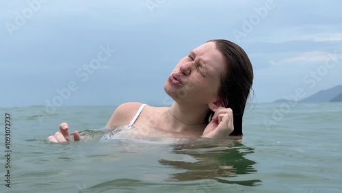 woman suffers from water getting into her ear in the sea during swimming