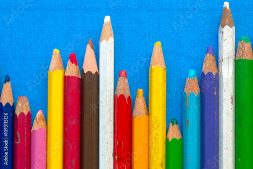 close up of colored wooden pencils in a row, on blue background. top view