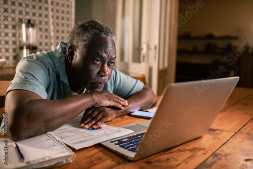 Senior black man looking stressed while using laptop at home