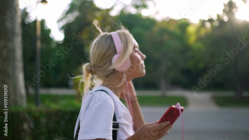 Young woman enjoying music in a park, wearing headphones and relaxing under the sunny sky during a summer day