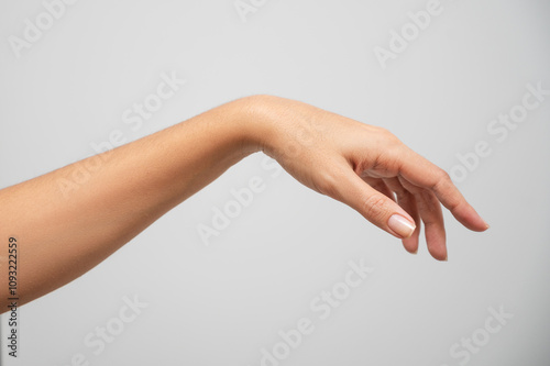 Close-up of an elegant female hand with neutral nail polish against a plain background, showcasing graceful fingers and smooth skin.