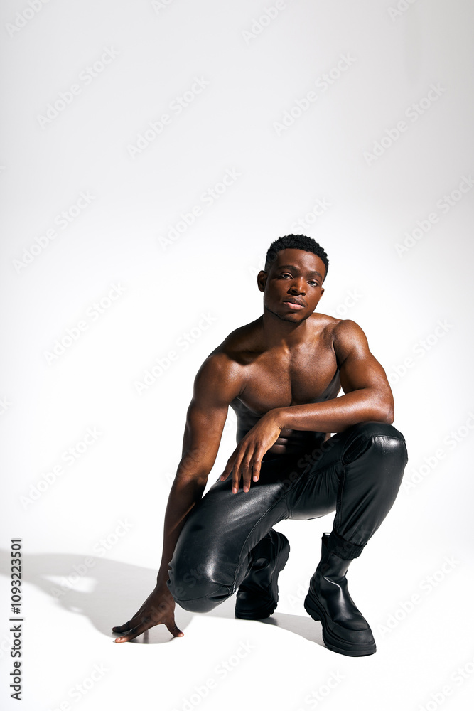A young handsome African American man strikes a powerful pose, wearing sleek black pants and bold boots. A young handsome African American man strikes a powerful pose, wearing sleek black pants and bold boots.