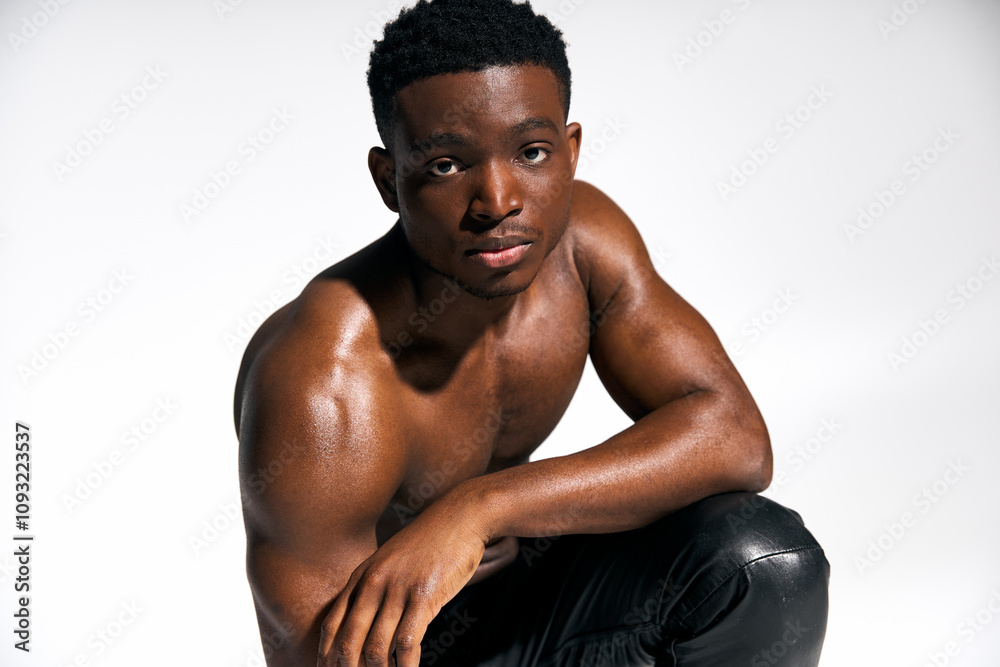 A young, attractive African American man poses topless with a relaxed yet confident expression. His strong physique is emphasized in the well lit studio setting, highlighting his charisma. A young, attractive African American man poses topless with a relaxed yet confident expression. His strong physique is emphasized in the well lit studio setting, highlighting his charisma.