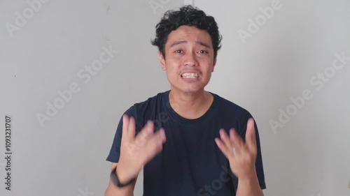 Man Explaining and rejected Gestures. A man stands indoors in front of a white wall, talking and gesturing with his hands.