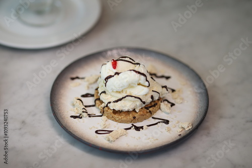 Delicious ice cream served on a crumbly cookie base, drizzled with chocolate syrup and topped with a cherry, presented on a stylish ceramic plate.