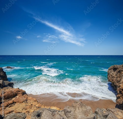 Shore sandy lonely beach with waves and ocean foam under summer blue sky. Peaceful nature seascape. Beautiful summer scenery and rocks on the sand. Wallpaper of atlantic ocean. Coast and Sea