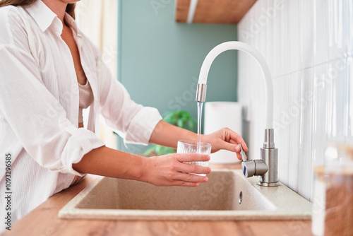 Obraz na plátně Woman fills a glass with clean filtered tap water for drinking in scandinavian s