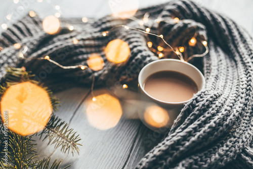 Winter cozy composition of a gray woolen scarf, coffee cup, and Christmas tree branches. Selective focus.