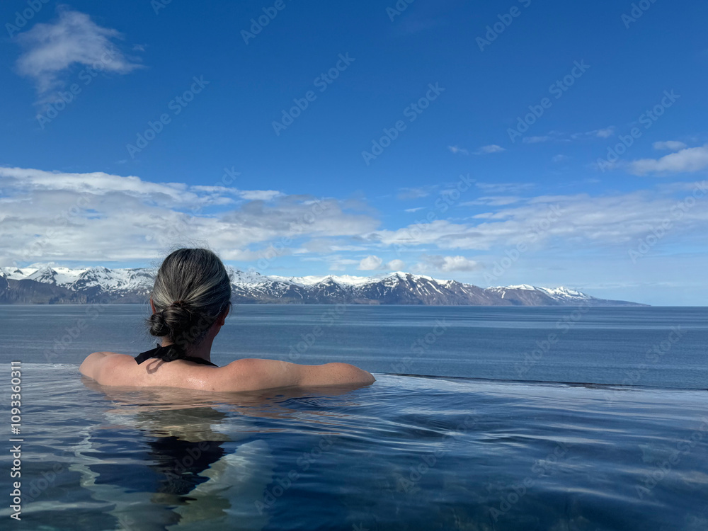 woman enjoying the view over the bay and the snow capped mountains in the distance while bathing in a geothermal hot pool woman enjoying the view over the bay and the snow capped mountains in the distance while bathing in a geothermal hot pool