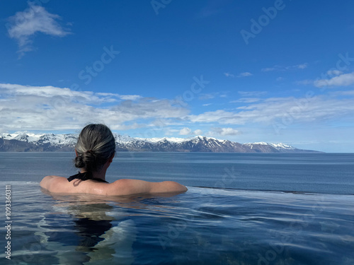 woman enjoying the view over the bay and the snow capped mountains in the distance while bathing in a geothermal hot pool