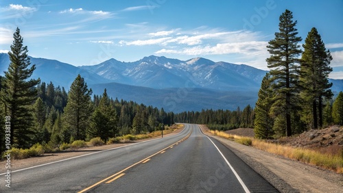 Empty stretch of asphalt road running parallel to a mountain range with a clear blue sky above and pine trees in the foreground, peaceful scene, road to nowhere, scenic beauty, natural landscape