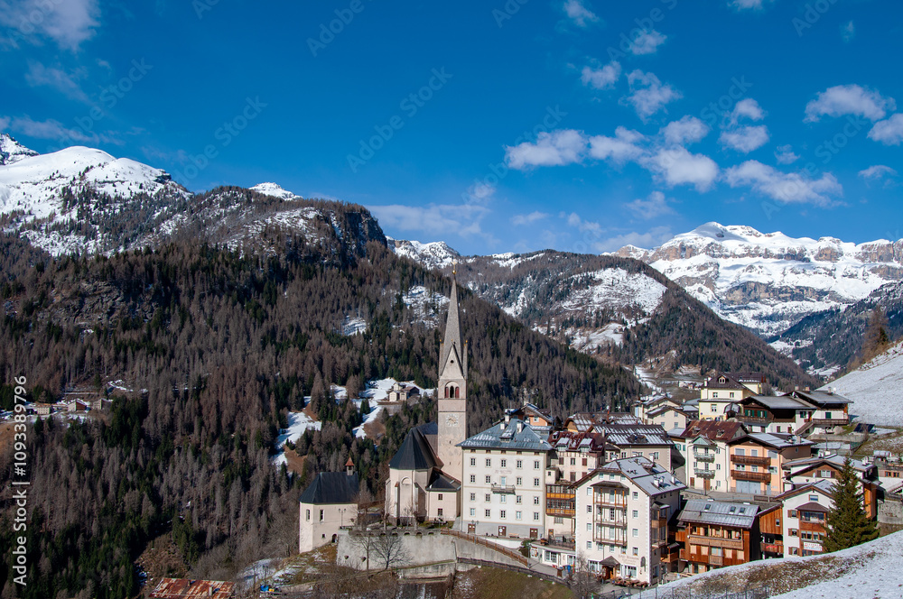 Dolomites, Italy. Pieve di Livinalongo village with church and houses near Arabba ski resort. Sella mountain massif in the background on the right