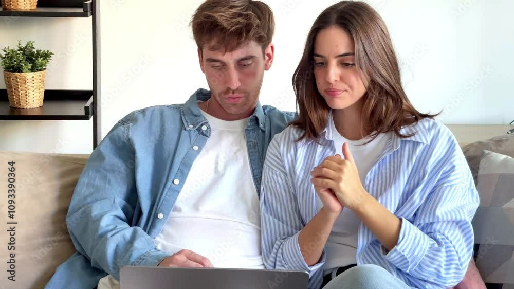 The couple is sitting on a couch in their living room, sharing the moment of reading disappointing results from an exam or work evaluation, feeling disappointed and uncertain. Problems online economy The couple is sitting on a couch in their living room, sharing the moment of reading disappointing results from an exam or work evaluation, feeling disappointed and uncertain. Problems online economy