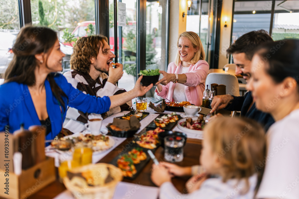 Obraz premium Family and friends gathered in a restaurant to eat delicious food, talk, drink and hang out.