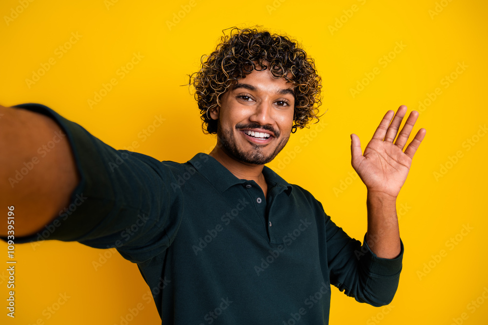 Happy young man waving hand against a vibrant yellow background wearing a stylish black shirt