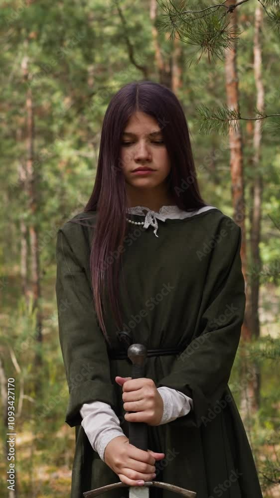 dark-haired young woman in forest plunges sword into ground dark-haired young woman in forest plunges sword into ground