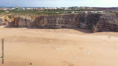 Aerial view of hundreds of surfers in the water, in South of Portugal, Sagres, Tonel Beach. Turquoise water. Famous travel destination. High cliff. Drone backwards above the bay.
