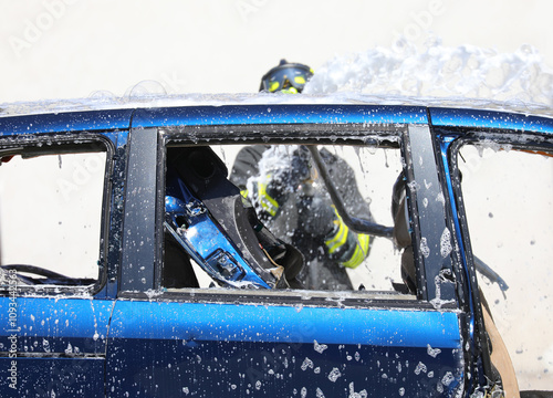 fire hose spraying white foam on the blue car after the road accident