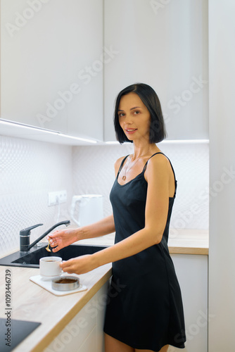 In a sleek, contemporary kitchen, a woman stands by the counter, holding a cup of coffee and a plate