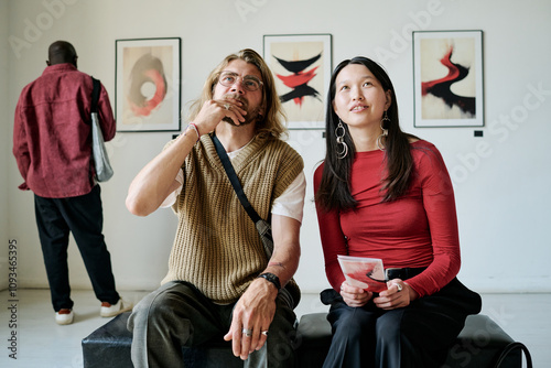 Group of diverse individuals observing artwork at an exhibition with focused, contemplative expressions, indicating interest in the displayed art pieces in background photo