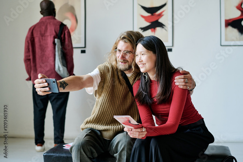 Fotografie Smiling friends taking selfie in modern art gallery, enjoying artwork in backgro