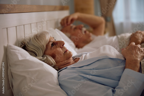 Thoughtful senior woman lying down in bed.