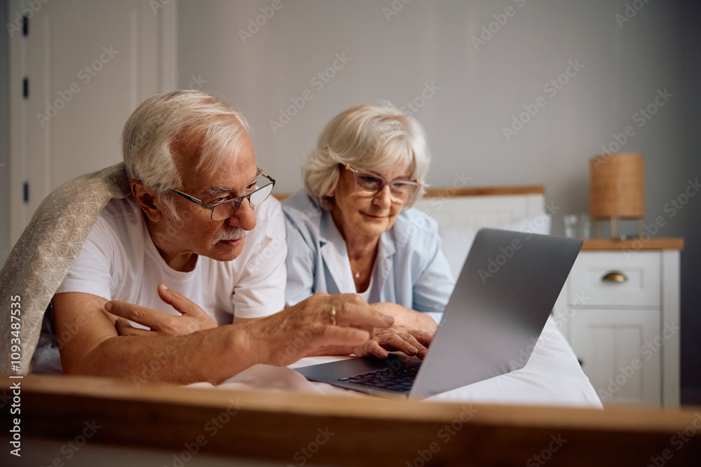 Senior couple using laptop while relaxing on bed. Senior couple using laptop while relaxing on bed.