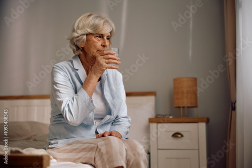 Pensive senior woman having  glass of water in bedroom. photo