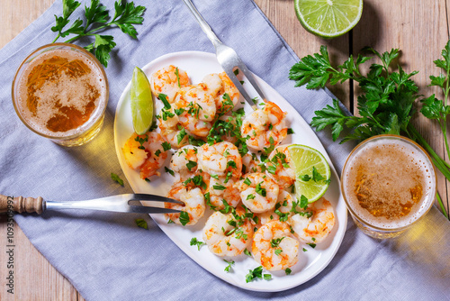 Shrimp cooked with garlic and herbs, served with beer and lime on a wooden table.