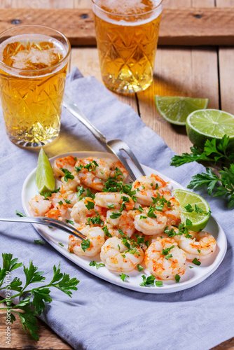 Shrimp cooked with garlic and herbs, served with beer and lime on a wooden table.