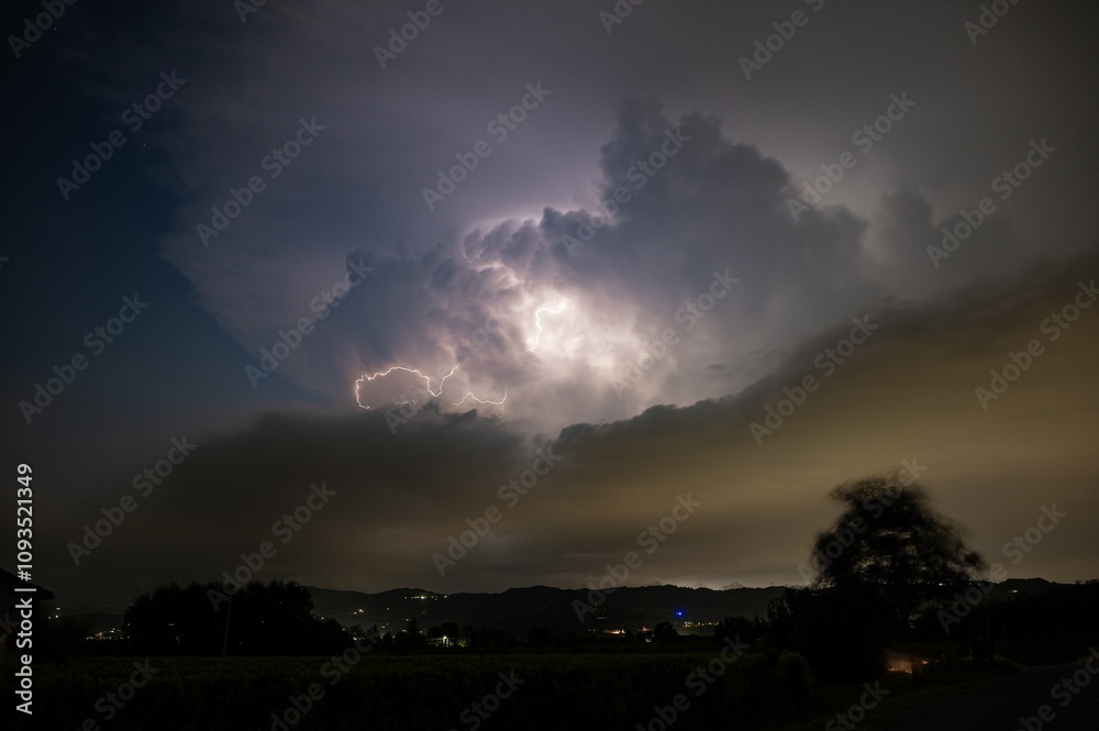 Supercell thunderstorm in the Po Valley, Italy is illuminated by lightning. Blurred tree due to high winds. Supercell thunderstorm in the Po Valley, Italy is illuminated by lightning. Blurred tree due to high winds.