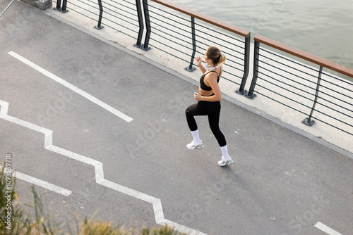 A young woman enjoys a serene morning run along the riverbank promenade, surrounded by modern architecture photo