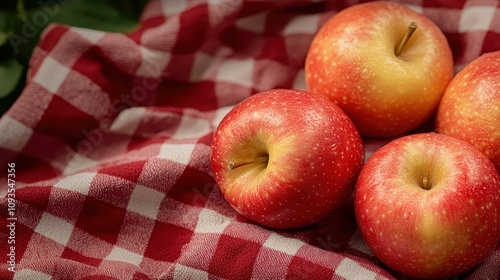 Four ripe red apples sit on a classic red and white checkered cloth, creating a rustic, fresh invitation to enjoy the simplicity of natural fruit and country decor. photo