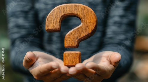 A wooden question mark is held gently by a pair of open hands against a soft grey background, symbolizing curiosity, inquiry, and the quest for knowledge in life’s journey. photo