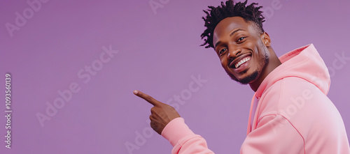 A young, happy Black man in a pink hoodie points at the empty space on a purple background