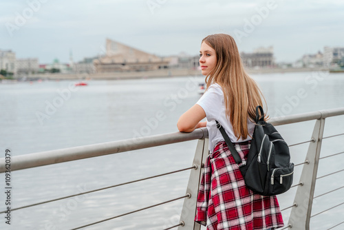 Portrait of a beautiful young girl with a backpack in a city park by the lake.